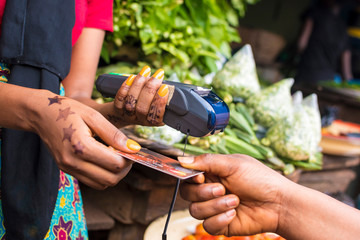 Poster - close up of an african woman selling in a local african market holding a mobile point of sale device collecting a credit card from a customer