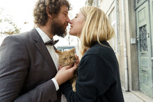Loving Couple Long-haired Blonde And Curly Man Standing On The Street With A Red Cat, Hiding Behind A Large White Hat. Fun Wedding Walking Concept. Happy Holiday Celebration.