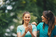 © Sanja - Two cute Caucasian women listening to music on smart-phone while walking through the park.