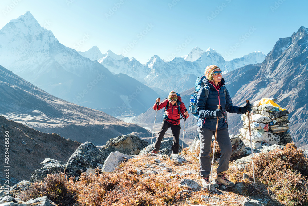 Couple following Everest Base Camp trekking route near Dughla 4620m. Backpackers carrying Backpacks and using trekking poles and enjoying valley view with Ama Dablam 6812m peak - obrazy, fototapety, plakaty 