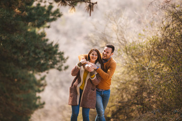 Playful young couple having fun, embracing and walking through woods.