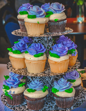 A Tower Of Vanilla And Chocolate Cupcakes Topped With Violet Blue Vanilla Frosting Shaped In Rosettes.