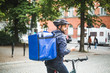 © Maskot - Food delivery man with bicycle looking away while standing on street in city