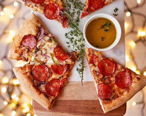 Christmas and New Year atmosphere. Hot Italian pizza with melting tomato, pepperoni and cheese on a white marbel cutting board. Background with lights in bokeh and selective focus