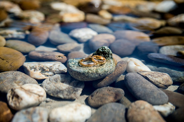 Wall Mural - wedding rings lie on the sea rock on water background. Wedding details concept. CLoseup