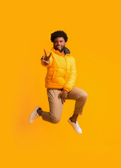Wall Mural - Positive winter black guy greeting with peace gesture while jumping