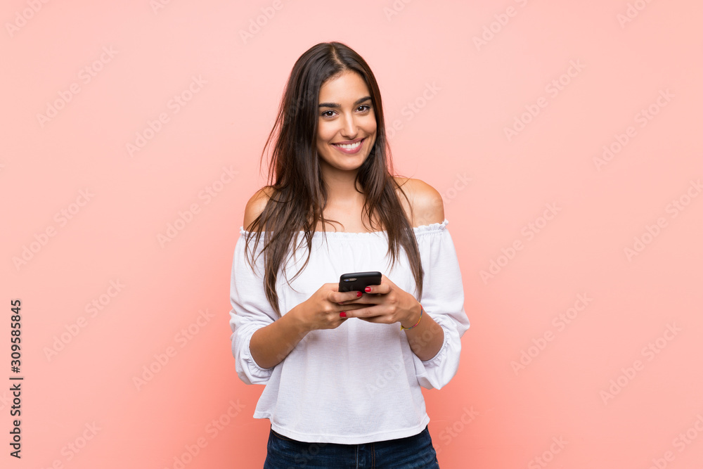 Young woman over isolated pink background sending a message with the mobile - obrazy, fototapety, plakaty 