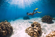 © artifirsov - Free diver young girl with yellow fins glides over sandy bottom and corals.