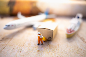 Miniature people: Worker and brown paper box on world map with airplane, ship using as background business shipping, rent container, worldwide transportation concept