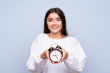 Wall Mural - Young woman over isolated blue background holding vintage alarm clock