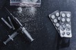 The concept of drug dependence, addiction. Scattered cocaine or heroin powder, syringes and blister with pills on black background top view