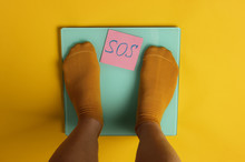 Female Legs In Socks Are Standing On The Floor Scales Against Yellow Background. Top View
