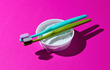 Two toothbrushes, tooth powder on pink neon background. Minimalism oral hygiene concept