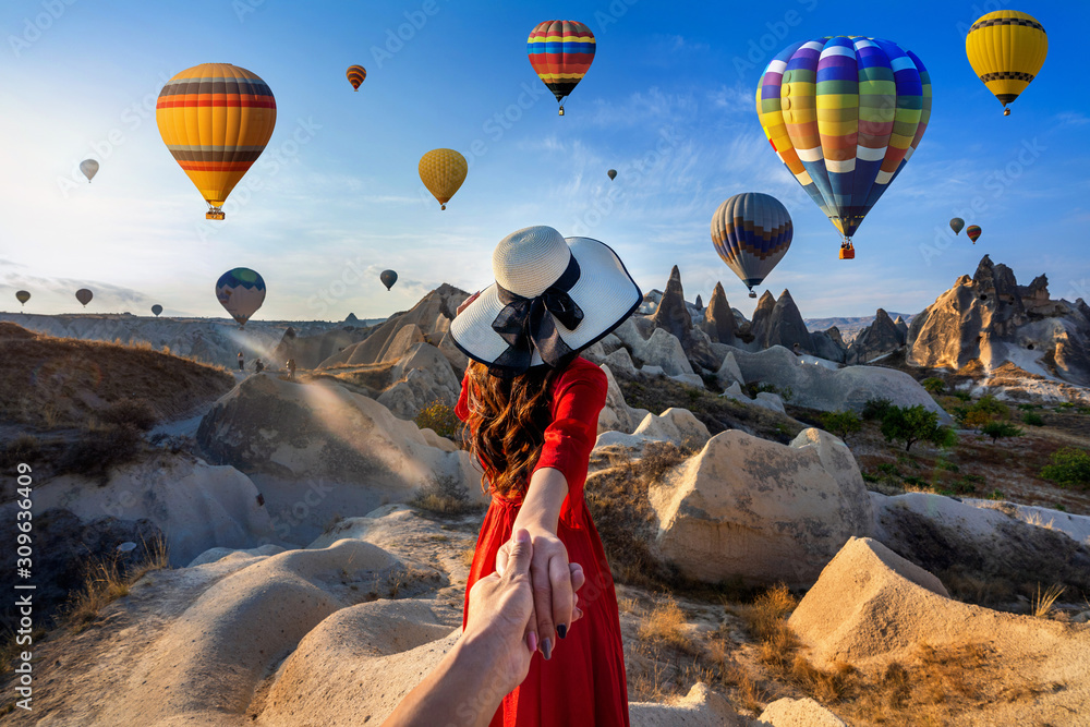 Women tourists holding man's hand and leading him to hot air balloons in Cappadocia, Turkey. - obrazy, fototapety, plakaty 
