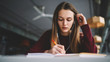 © GalakticDreamer - Smart woman enjoying new playlist by headphones while writing interesting ideas to notebook, pensive attractive student learning at college library listening songs and records for concentration