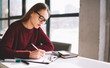 © GalakticDreamer - Young concentrated female student sitting in university cafe and drawing sketch, serious pensive woman in eyeglasses writing essay pondering about idea, casual skilled girl using notepad for planning