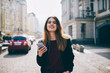 © GalakticDreamer - Portrait with happy young hipster girl holding modern smartphone in hand looking at camera walking on street, attractive female blogger using cellular for chatting while browsing 4g internet in city