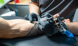 Fototapeta Konie - Male arm with tattoo. Master in black gloves is preparing to draw new tattoo. Tattoo machine.