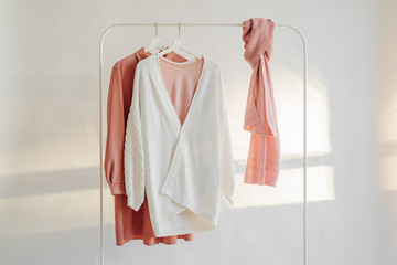 Wall Mural - Female clothes in pastel pink color on hanger on white background. Elegant dress, jumper, shirt and scarf. Spring cleaning home wardrobe. Minimal concept.
