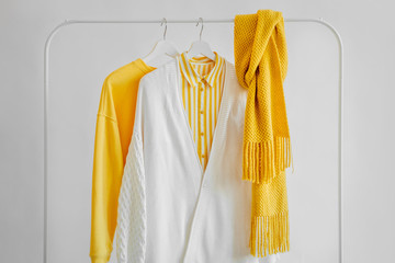 Wall Mural - Female clothes in yellow color on hanger on white background. Jumper, striped shirt and scarf. Spring/autumn outfit. Minimal concept.