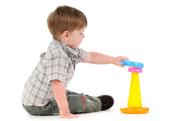 Pretty one year little baby playing with colorful pyramid. Child sits and holds loved toy portrait on light background