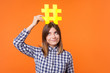 © khosrork - Popularity in social media. Portrait of funny brunette woman wearing checkered casual shirt holding large big yellow hashtag sign on head as crown. indoor studio shot isolated on orange background