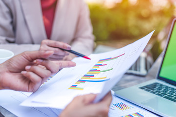 Two business women review and analyzing income charts and graphs with modern laptop computer. Close up businesswomen finger pointing to graph. Business analysis and strategy concept.