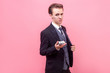 © khosrork - Portrait of arrogant rich businessman in elegant suit and with stylish haircut showing bunch of dollars on camera, offering money or boasting earnings. indoor studio shot isolated, pink background