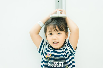 Wall Mural - Little asian girl measuring her height near white wall in hospital.5 years old girl kid standing and looking at above using hand measuring her height.