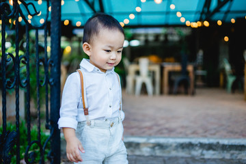 Funny 2 years old little asian baby boy wearing vintage clothes style and posing standing on the fence in english garden.film tone.