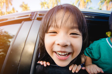 Wall Mural - Happy siblings laughing and smiling near window go travel by car against blue sky and coconut trees.Summer road trip, Family with children in car.