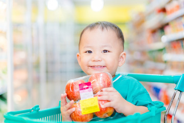 Wall Mural - Funny little asian boy child smile and laughing in hypermarket, little asian toddler boy sitting in the trolley cart during family shopping in supermarket.