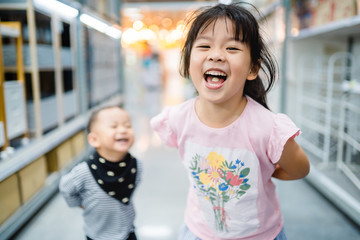 Wall Mural - Little sister playing and running with her brother in Supermarket.Toddler kids sibling going shopping in the Mall.