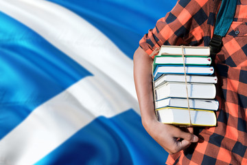 Scotland national education concept. Close up of teenage student holding books under his arm with country flag background.