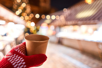 Hand holding a cup of mulled wine with blurred background of winter wonderland, a Christmas Market in European small city