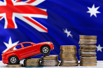 Australia savings concept. Money for new automobile, toy car and coin piles standing on national flag background. Copy space for text.