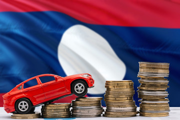 Laos savings concept. Money for new automobile, toy car and coin piles standing on national flag background. Copy space for text.