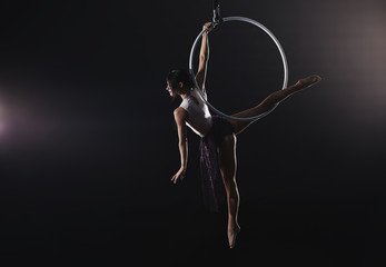 Poster - Young woman performing acrobatic element on aerial ring against dark background