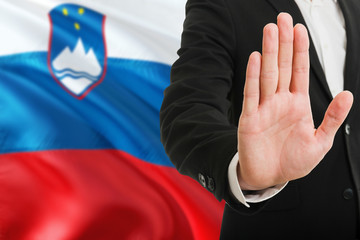 Wall Mural - Slovenia rejection concept. Elegant businessman is showing stop sign with hand on national flag background.