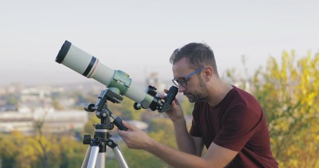 Wall Mural - astronomer with a telescope watching at the stars and moon with blurred city background.