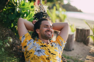 Wall Mural - A young man lies in a hammock on a sunny beach.