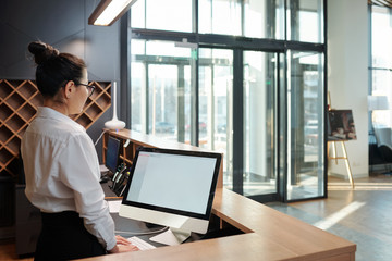 young female receptionist standing in front of computer screen by counter