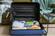 © Pixel-Shot - Open suitcase with packed clothes and accessories on floor at home