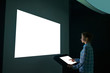 © zyabich - Mock up, futuristic, template, copyspace and education concept. Woman using interactive kiosk and looking at white blank large wall display in dark room of modern technology museum - mockup image