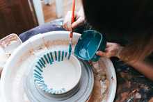 Professional Potter Works On Painting Plates In The Workshop. Woman Paints A Ceramic Plate With A Brush And Blue Paint