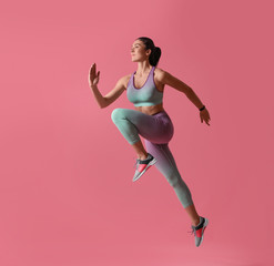 Canvas Print - Athletic young woman running on pink background, side view