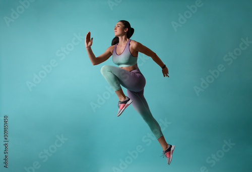 Cuadros en Lienzo Athletic young woman running on turquoise background, side view