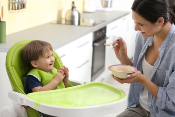 Wall Mural - Young nanny feeding cute little baby in kitchen