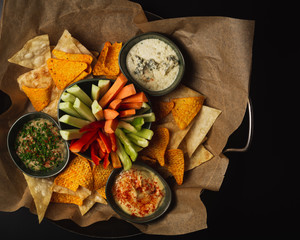 Chips and Dips Plate. on the dark background. Healthy Homemade Creamy Hummus and Babaganush with Olive Oil, assorted fresh vegetables and Pita Chips.