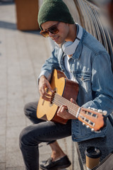 Smiling guitarist in hat playing song on the street